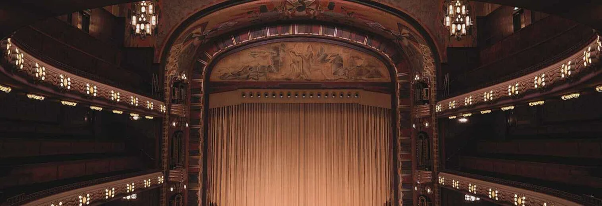 Bühne mit Vorhang und Ränge in dunkelbeleuchtetem Theater mit Kulturprogramm